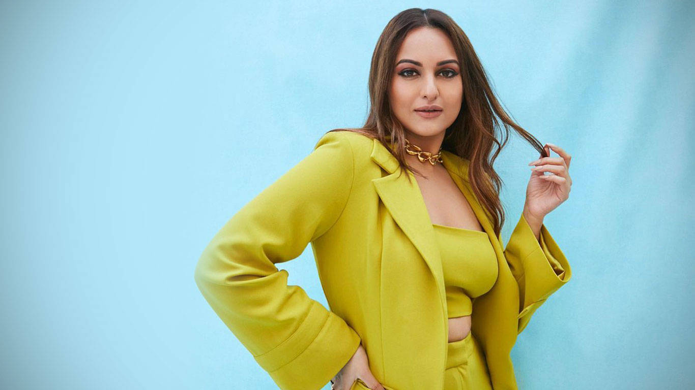 Sonakshi Sinha 桌布 壁紙 — 一位身穿大膽黃色西裝外套和配套上衣的女性，在柔和的藍色工作室背景前自信地擺姿勢。