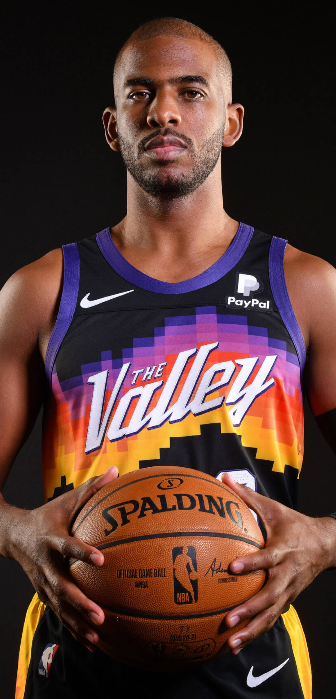Chris Paul 桌布 壁紙 — 一位身穿太陽隊球衣的籃球運動員，在黑色背景下專注地拿著一個Spalding籃球。