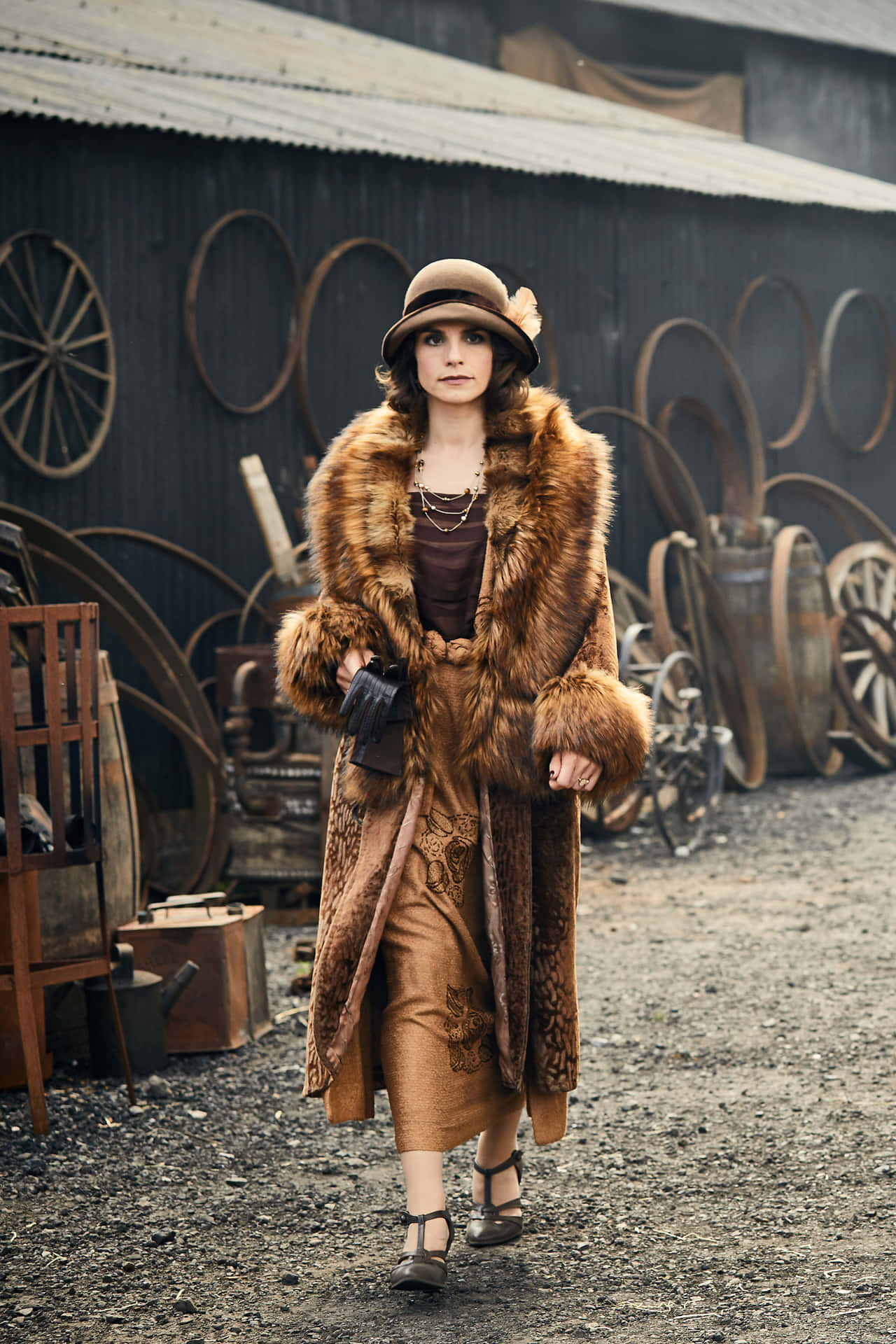 穿著復古皮草大衣和帽子的女性走過舊農場設備。 — Peaky Blinders 壁紙