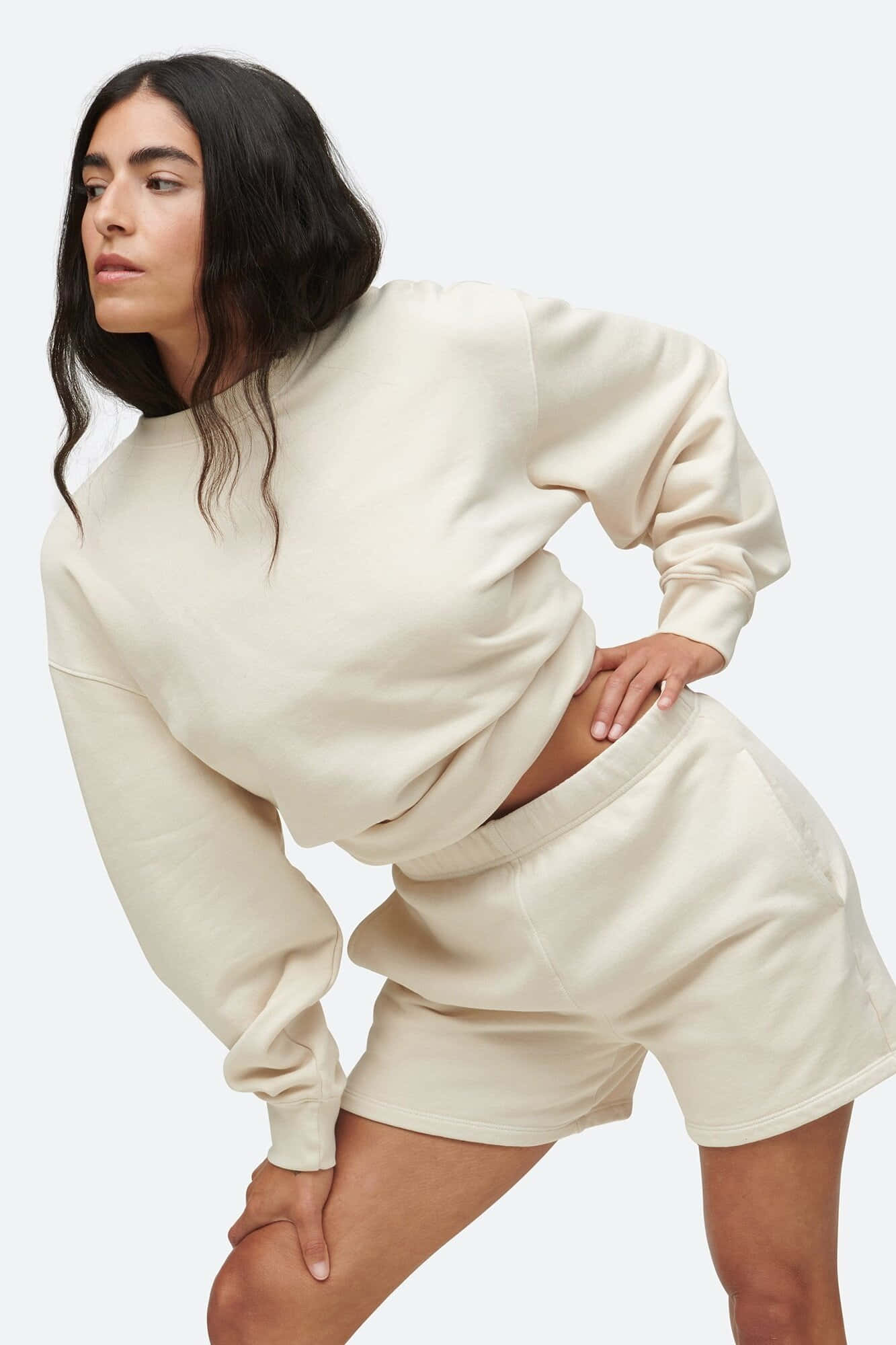 Minimalist Fashion 桌布 壁紙 — 一位身穿奶油色家居服的女性在純色淺色背景前自信地擺姿勢。