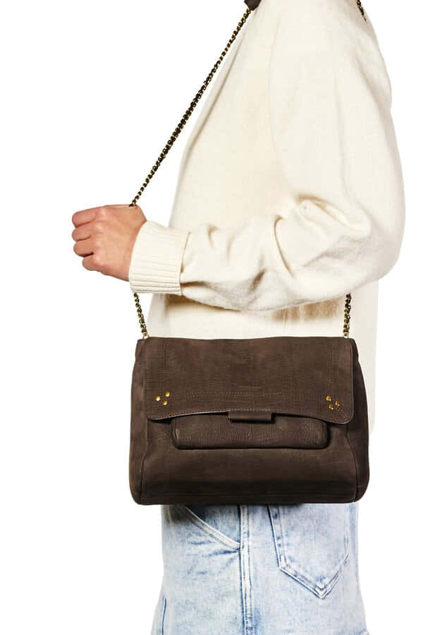 Handbag 桌布 壁紙 — 一位身穿奶油色毛衣和牛仔褲的人，背著一個帶金色鏈條的棕色麂皮斜挎包。