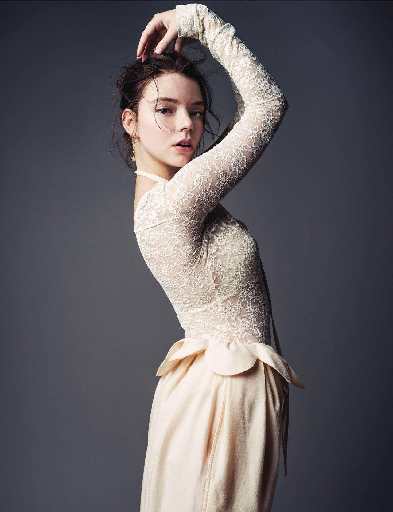 Anya 桌布 壁紙 — 一位身穿奶油色蕾絲上衣和飄逸裙子的女士，在深灰色工作室背景前優雅地擺姿勢，一隻手臂舉起。