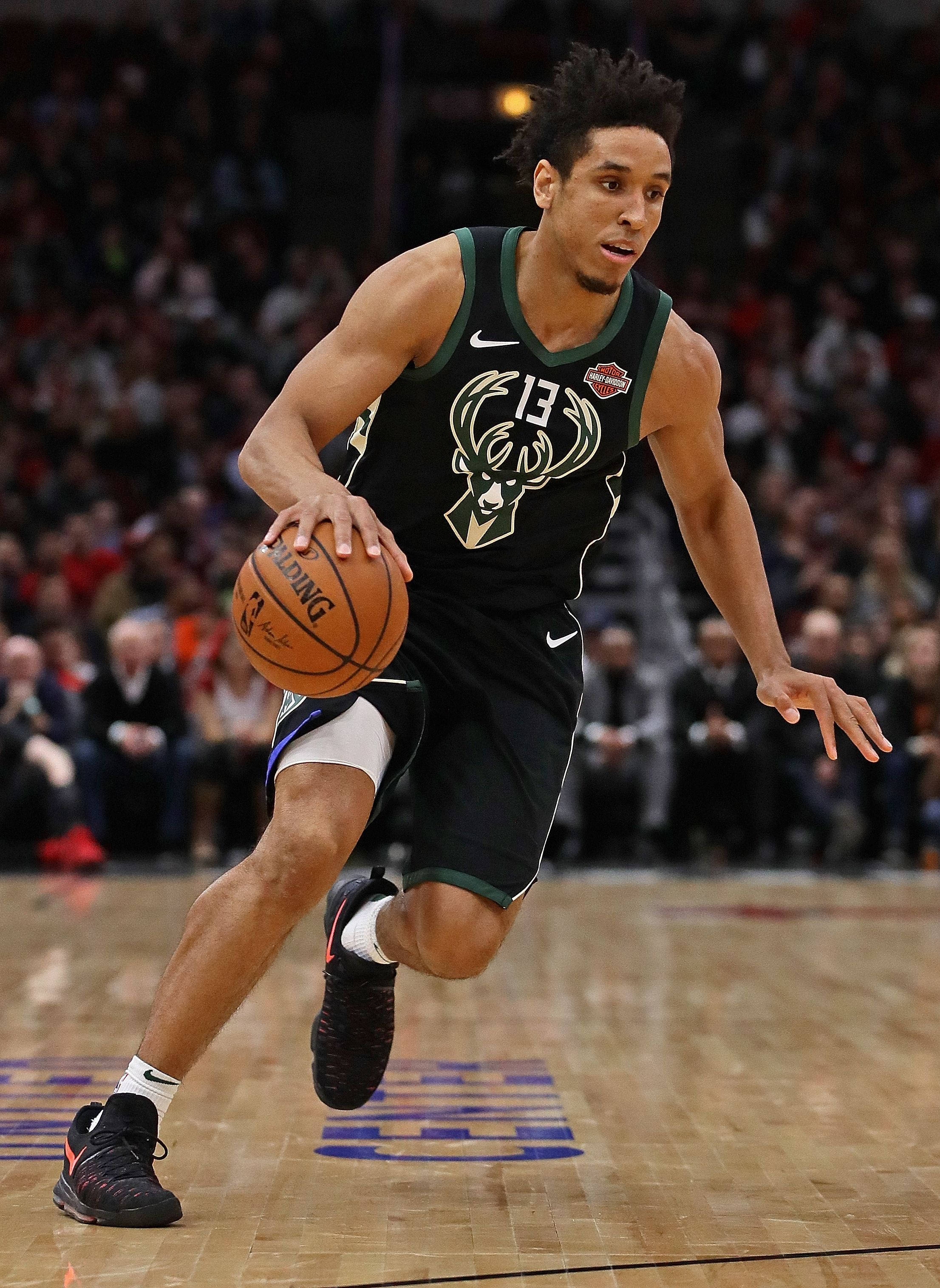malcolm brogdon 桌布 壁紙 — 一位身穿密爾瓦基公鹿隊球衣的籃球運動員，在明亮的場館燈光下，於激烈的比賽中專注地運球。