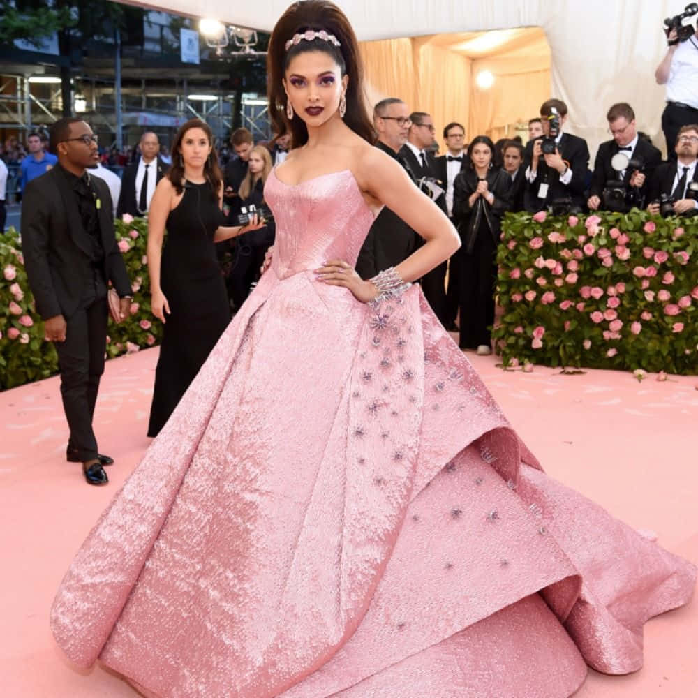 Met Gala 桌布 壁紙 — 一位身穿寬大粉紅色禮服的女士在粉紅色地毯上自信地擺姿勢，兩旁是攝影師和花籬。