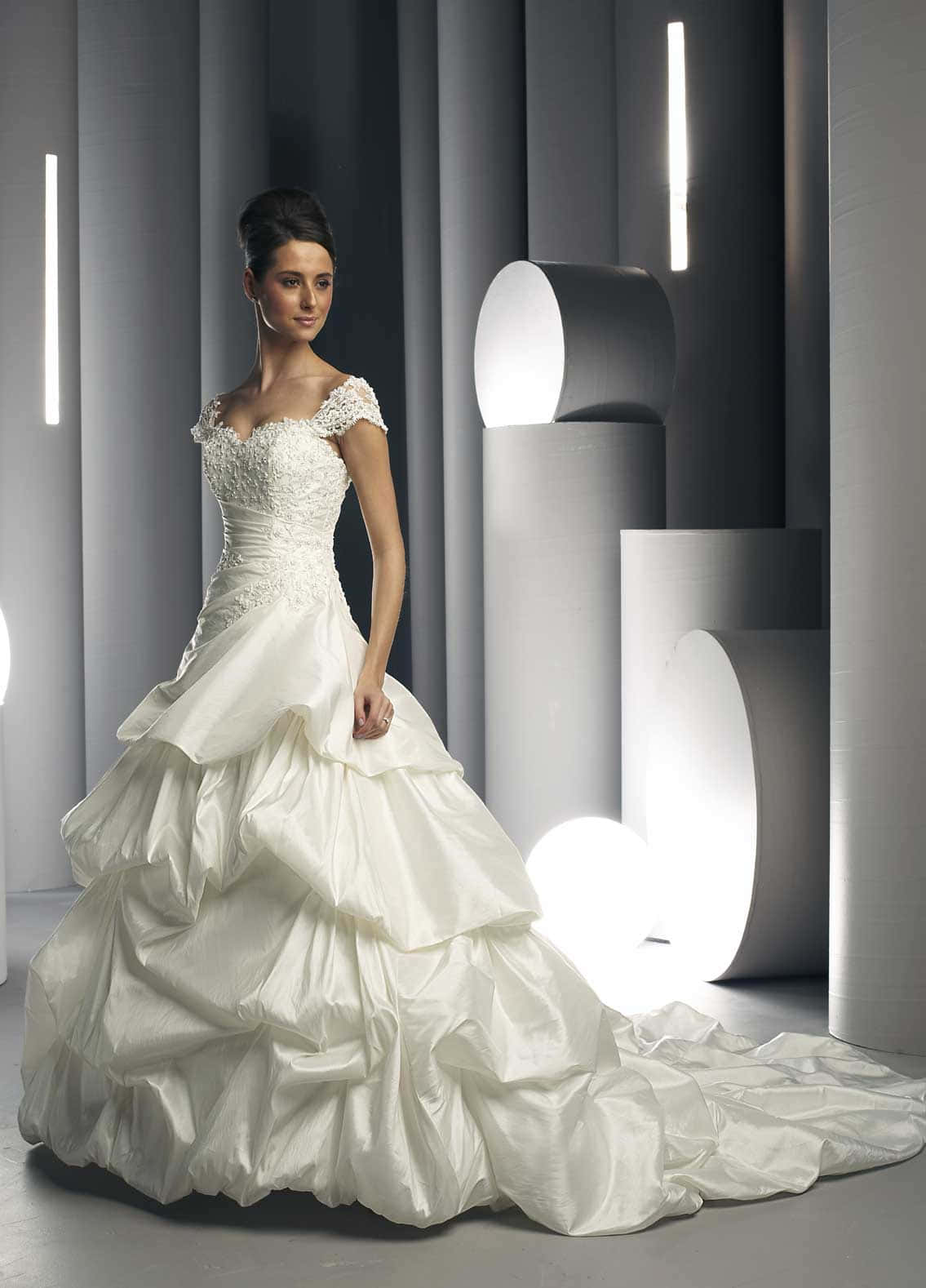 Wedding Gown 桌布 壁紙 — 一位身穿寬鬆白色婚紗的新娘，在一個極簡風格的攝影棚中，周圍有幾何灰色柱子和發光的垂直燈光。