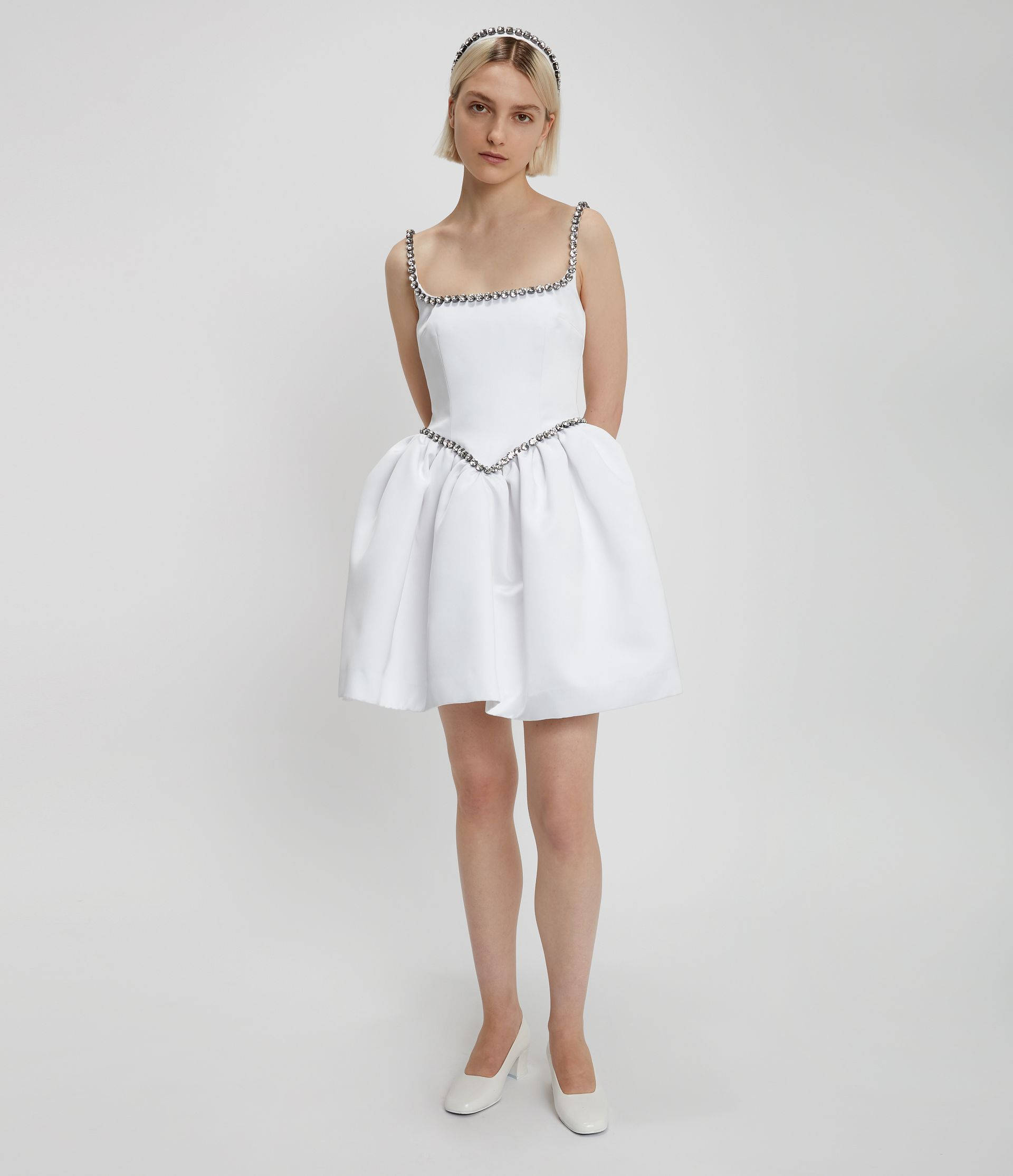 Clothes 桌布 壁紙 — 一位身穿帶有銀色鏈條裝飾的白色連衣裙的女性，在純白色背景前優雅地站立。