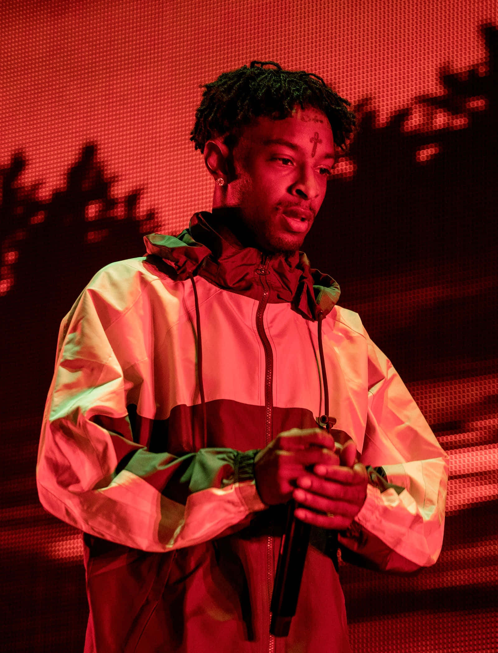 21 Savage 桌布 壁紙 — 一位身穿彩色外套的表演者在強烈的紅色舞台燈光下拿著麥克風，身後有陰影般的輪廓。