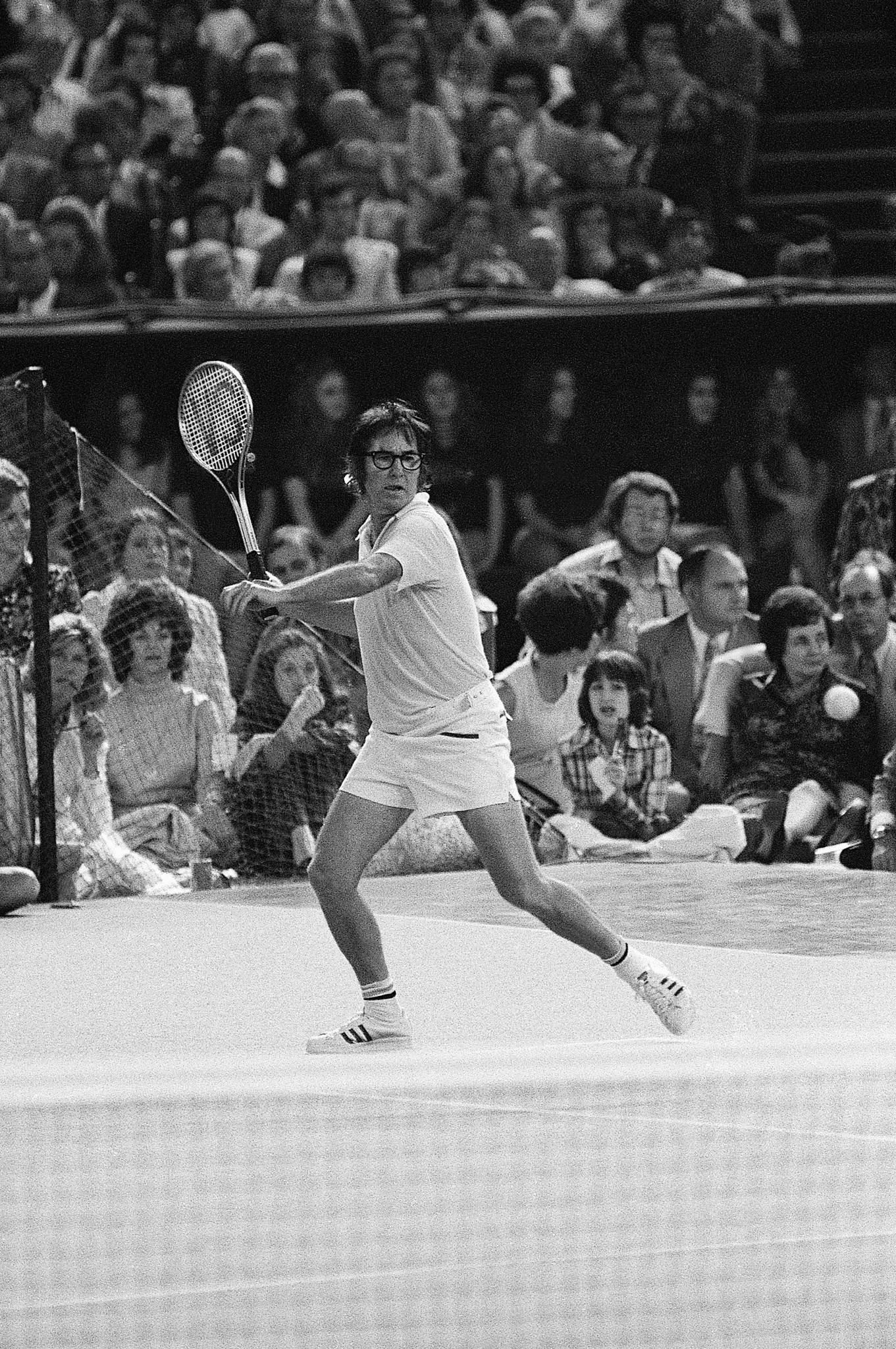 Tennis 桌布 壁紙 — 一位身穿復古白色裝備的網球選手在比賽中揮動球拍，觀眾在觀眾席上專注觀看。