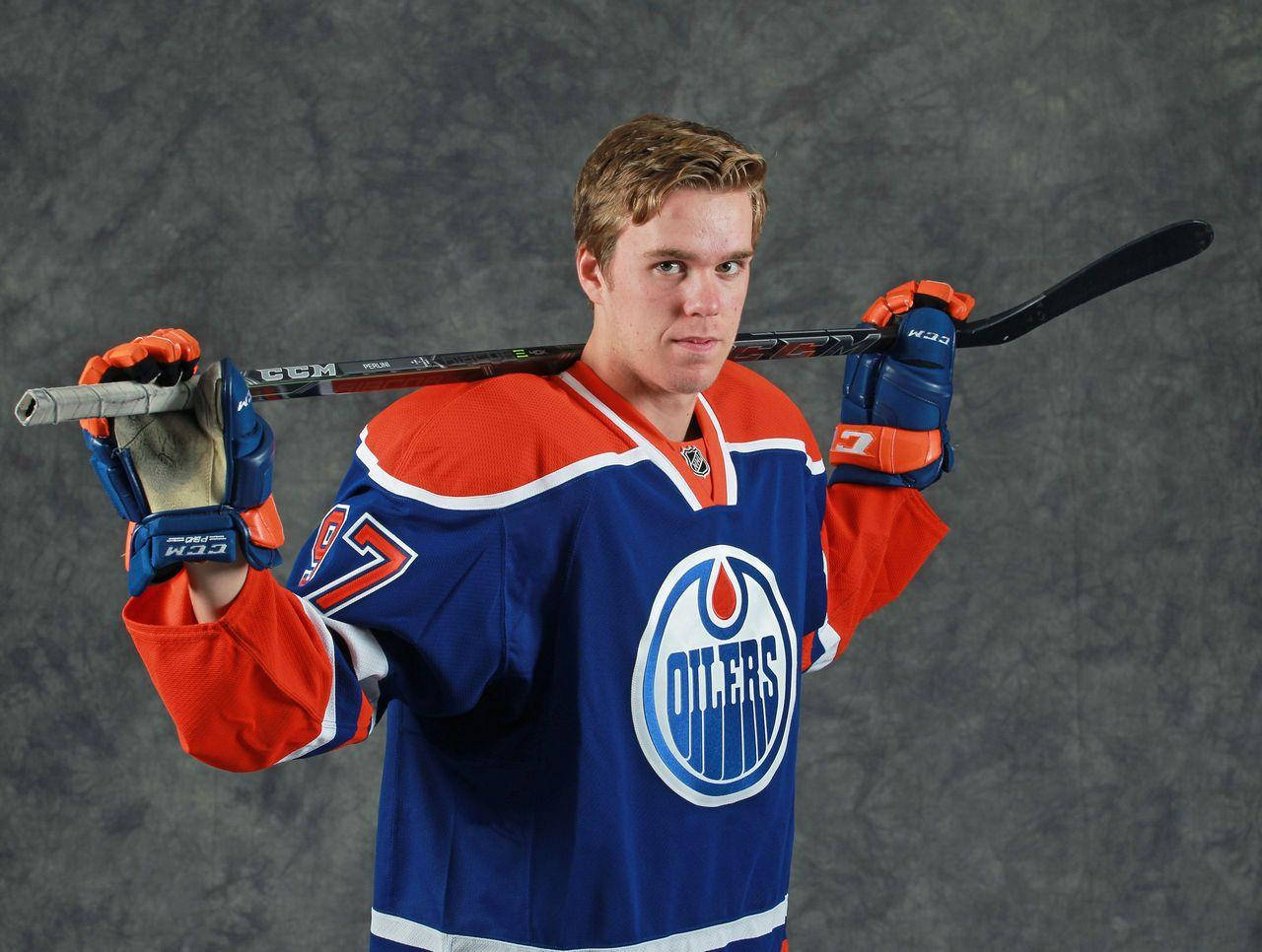 hockey 桌布 壁紙 — 一位身穿愛德蒙頓油人隊球衣的年輕冰球運動員，在灰色攝影棚背景下將球棒扛在肩上。