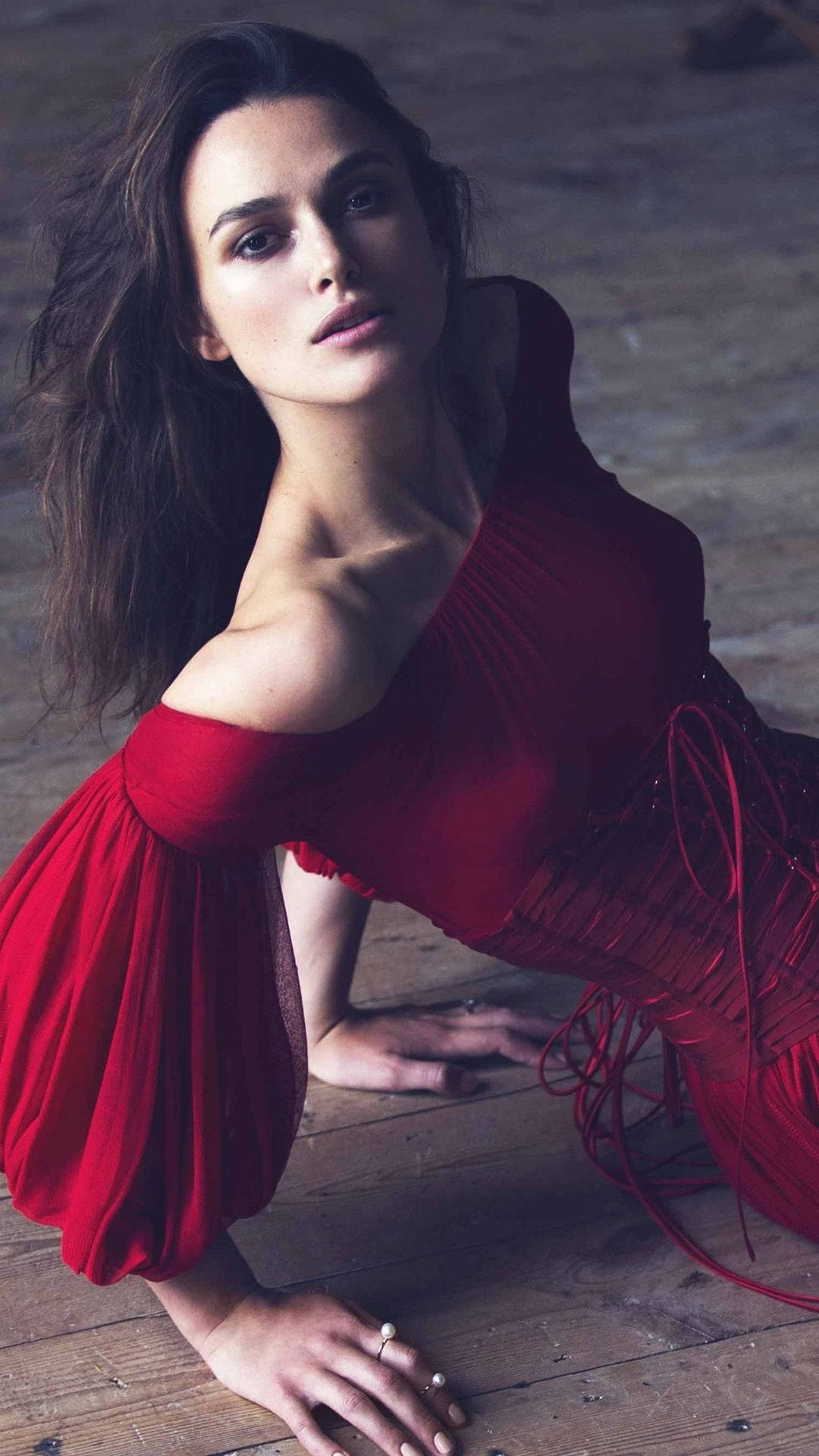 Keira Knightley 桌布 壁紙 — 一位身穿搶眼紅色露肩連衣裙的女性跪在風化的木地板上，目光專注。