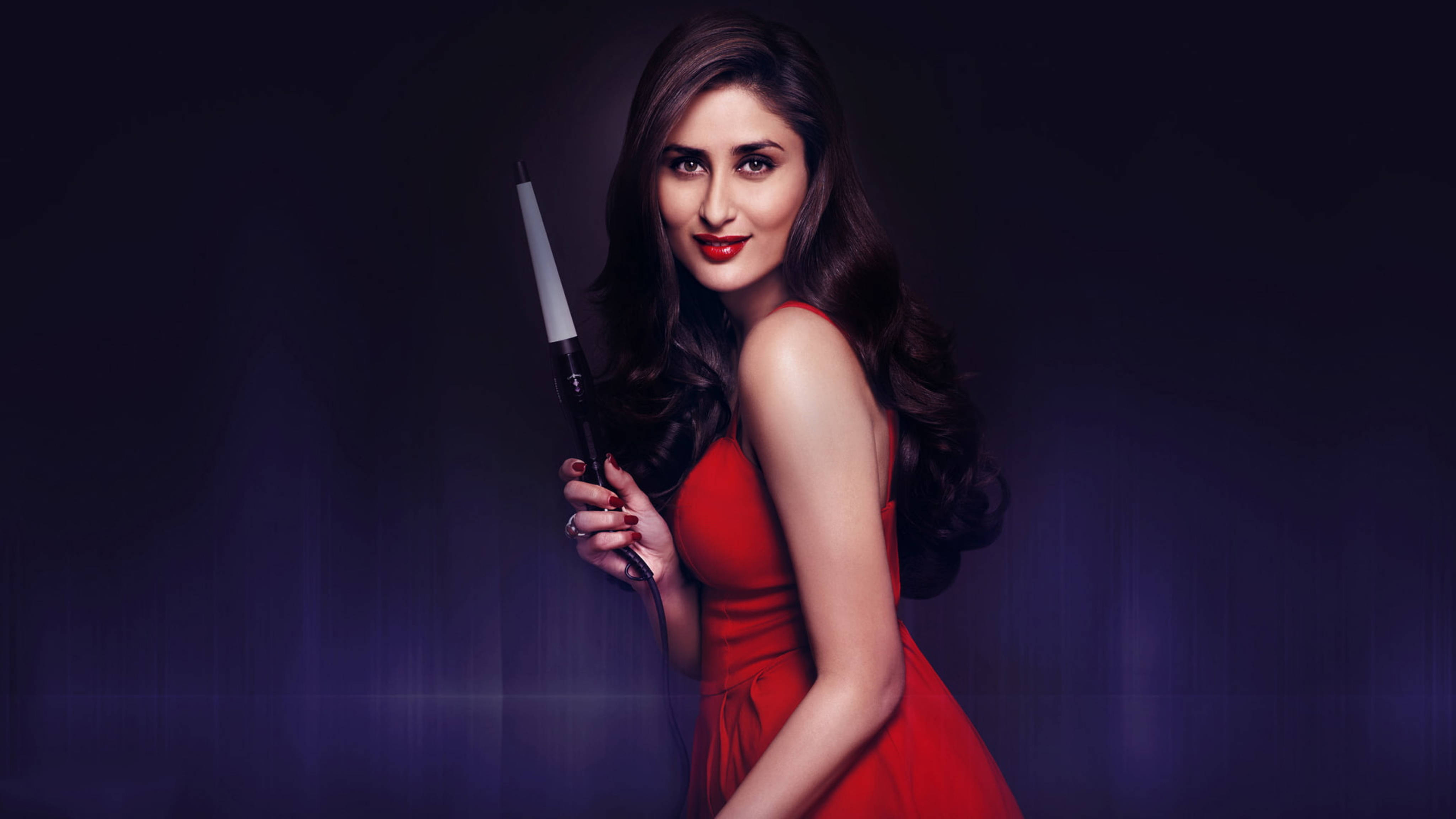 Kareena 桌布 壁紙 — 一位身穿搶眼紅裙的女性，在深紫色背景和戲劇性燈光下拿著捲髮棒。