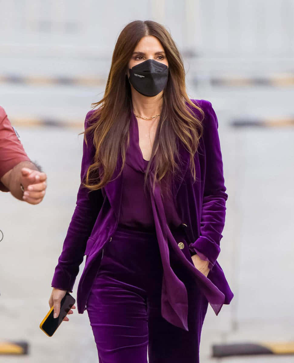 Sandra Bullock 2021 桌布 壁紙 — 一位身穿搶眼紫色天鵝絨西裝的女性自信地走著，同時戴著黑色口罩。
