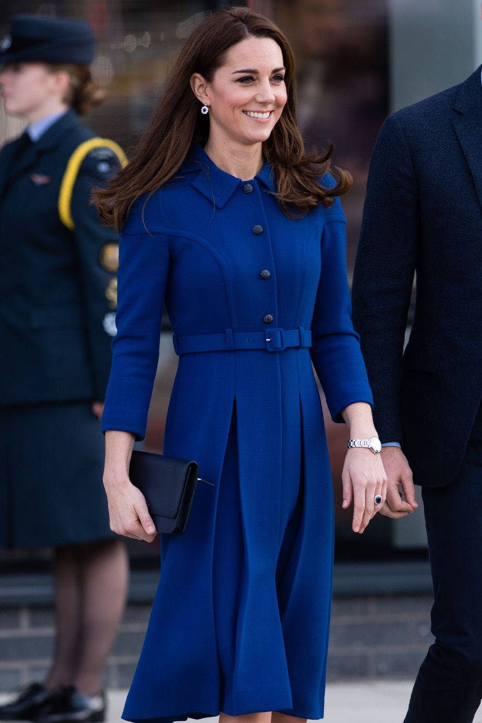Kate Middleton 桌布 壁紙 — 一位身穿搶眼鈷藍色外套連衣裙的女性微笑著，與一位身穿深色西裝的男士手牽手散步。