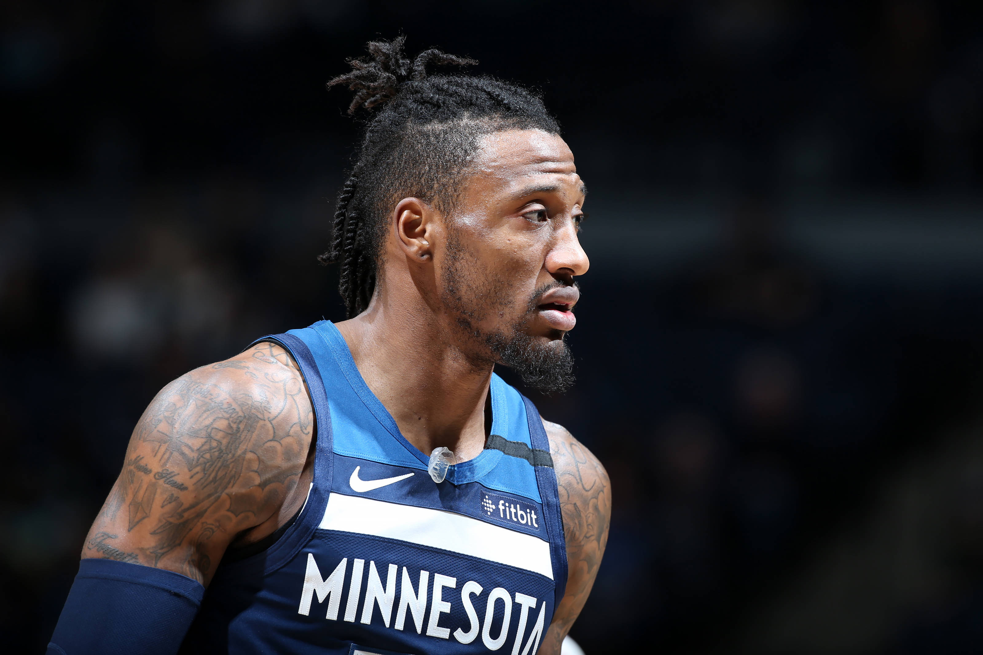 robert covington 桌布 壁紙 — 一位身穿明尼蘇達球衣、帶有刺青的專注籃球運動員，在場館燈光下比賽中凝視著。