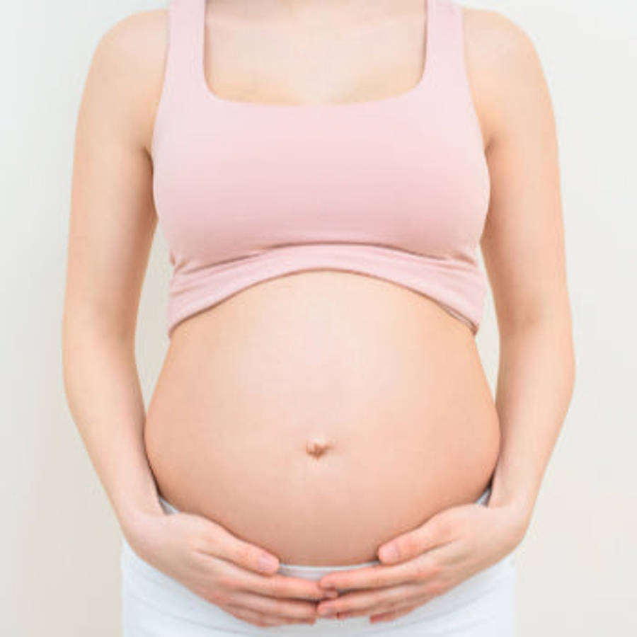 Pregnant 桌布 壁紙 — 一位身穿柔和粉紅色上衣的孕婦，在純色淺色背景前輕輕地捧著她圓潤的肚子。