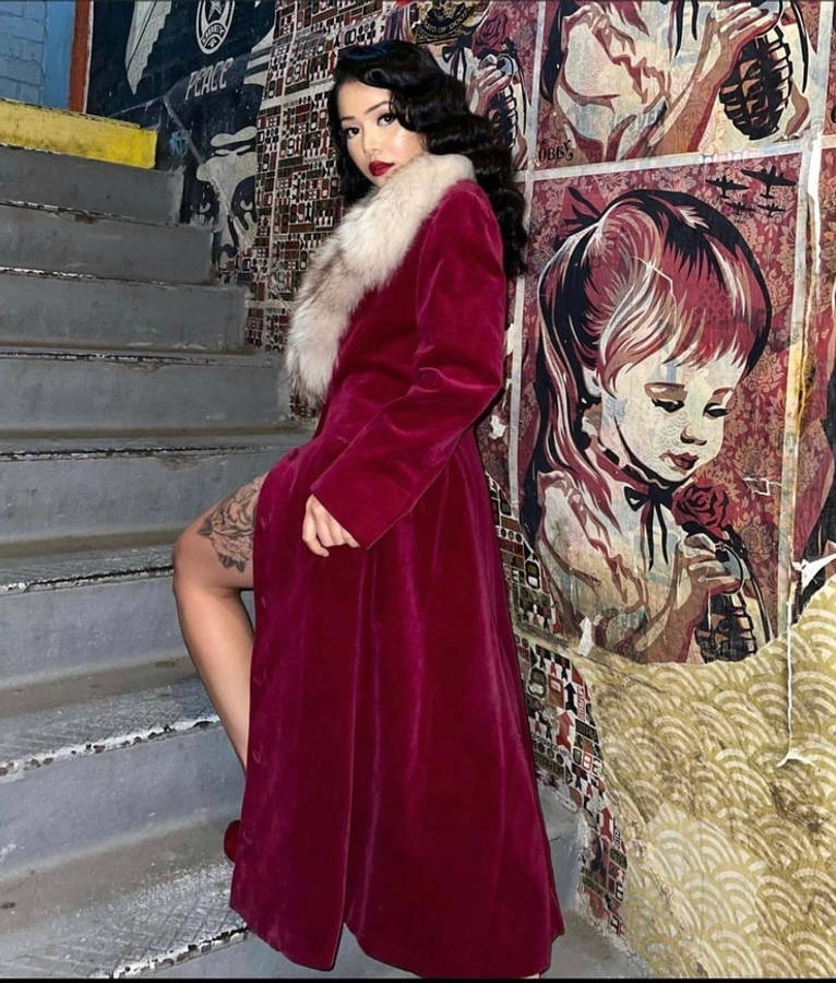 Bella Poarch 桌布 壁紙 — 一位身穿柔軟酒紅色外套、配有毛領的女性，坐在混凝土樓梯上，旁邊是一幅充滿活力的塗鴉壁畫。