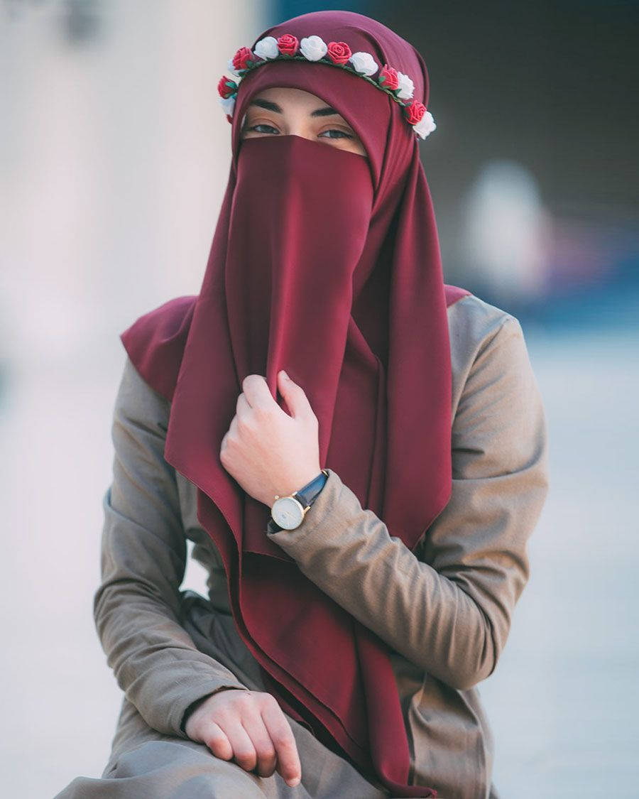 muslim 桌布 壁紙 — 一位身穿栗色尼卡布、頭戴花卉頭帶的女性，在戶外坐著，溫柔地凝視。