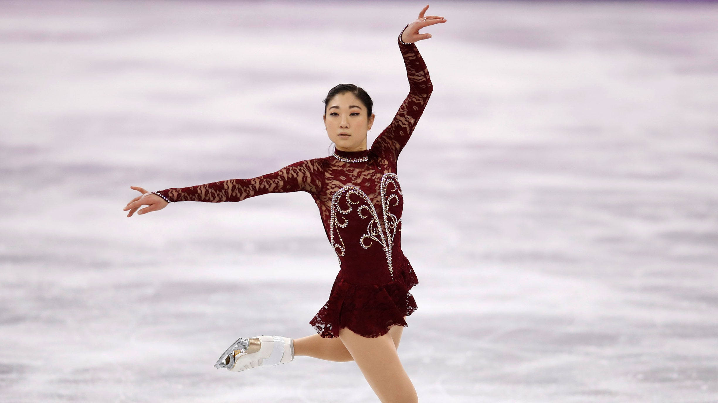 skate 桌布 壁紙 — 一位身穿栗色蕾絲服裝的女子花式滑冰運動員，單腿伸展，雙臂優雅地張開，在冰上優雅滑行。