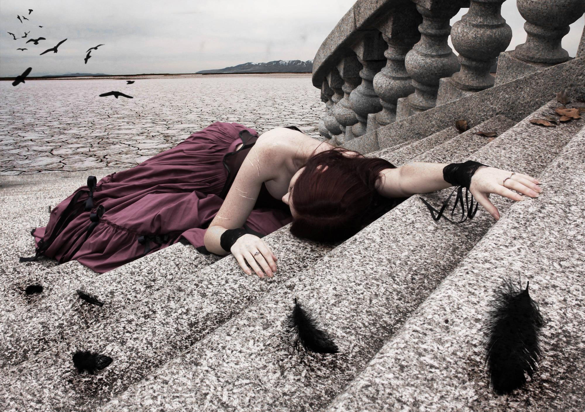 emo 桌布 壁紙 — 一位身穿栗色連衣裙的女性一動不動地躺在乾裂湖泊旁的石階上，黑色鳥兒在頭頂翱翔。
