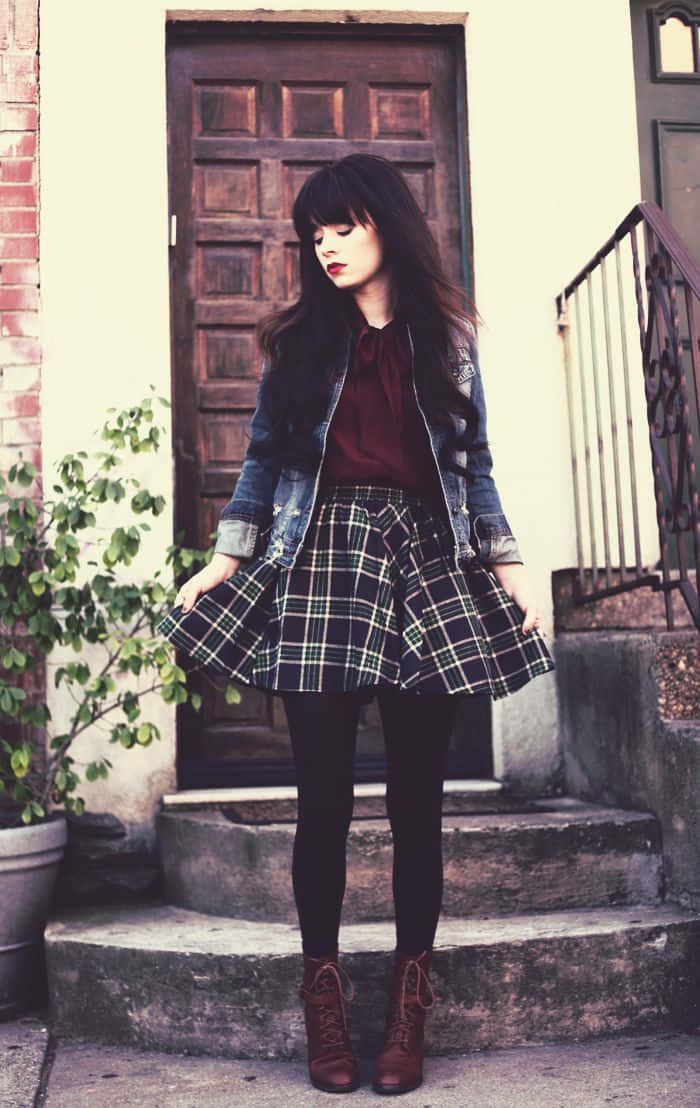 身穿格紋裙和牛仔外套的年輕女子站在戶外石階上。 — Emo 美學 GIF 壁紙