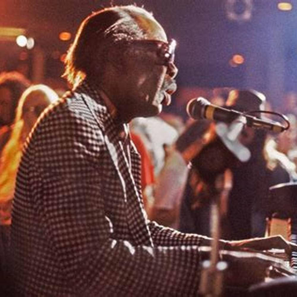 music festival 桌布 壁紙 — 一位身穿格紋襯衫、戴眼鏡的音樂家在溫暖的舞台燈光下，旁邊有麥克風，熱情地彈奏鋼琴。