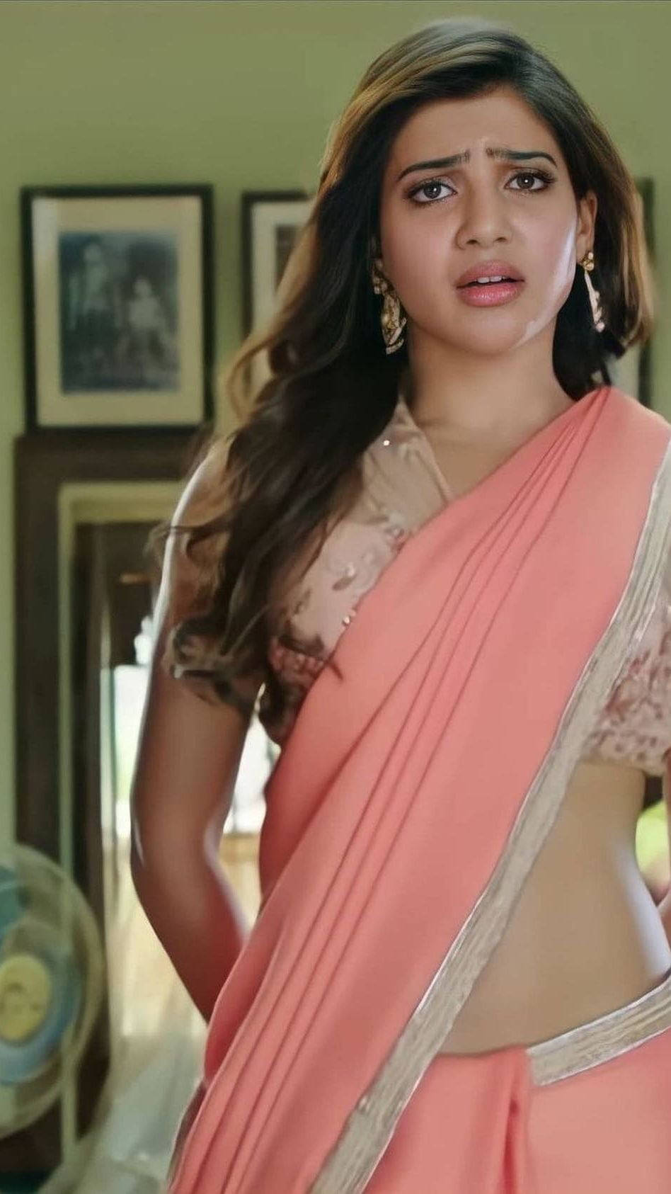 Samantha Saree 桌布 壁紙 — 一位身穿桃紅色銀邊紗麗的女性在室內顯得憂心忡忡，身後牆上掛著裱框照片。