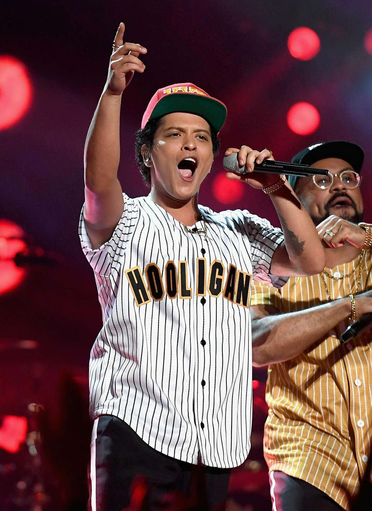 Bruno 桌布 壁紙 — 一位身穿條紋 'HOOLIGAN' 球衣的男歌手在紅燈光下與樂隊成員一起熱情表演。