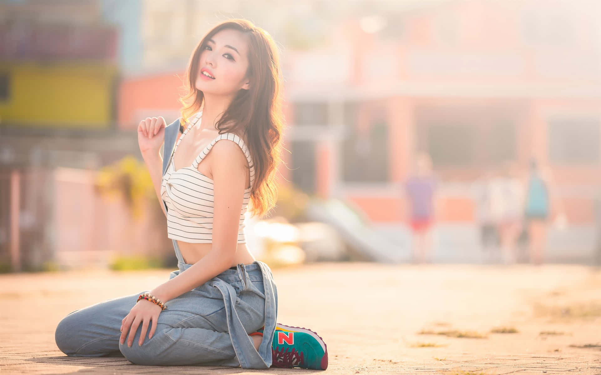 女孩 桌布 壁紙 — 一位身穿條紋上衣和牛仔褲的年輕女子跪在人行道上微笑，金色的陽光灑在她的頭髮上。