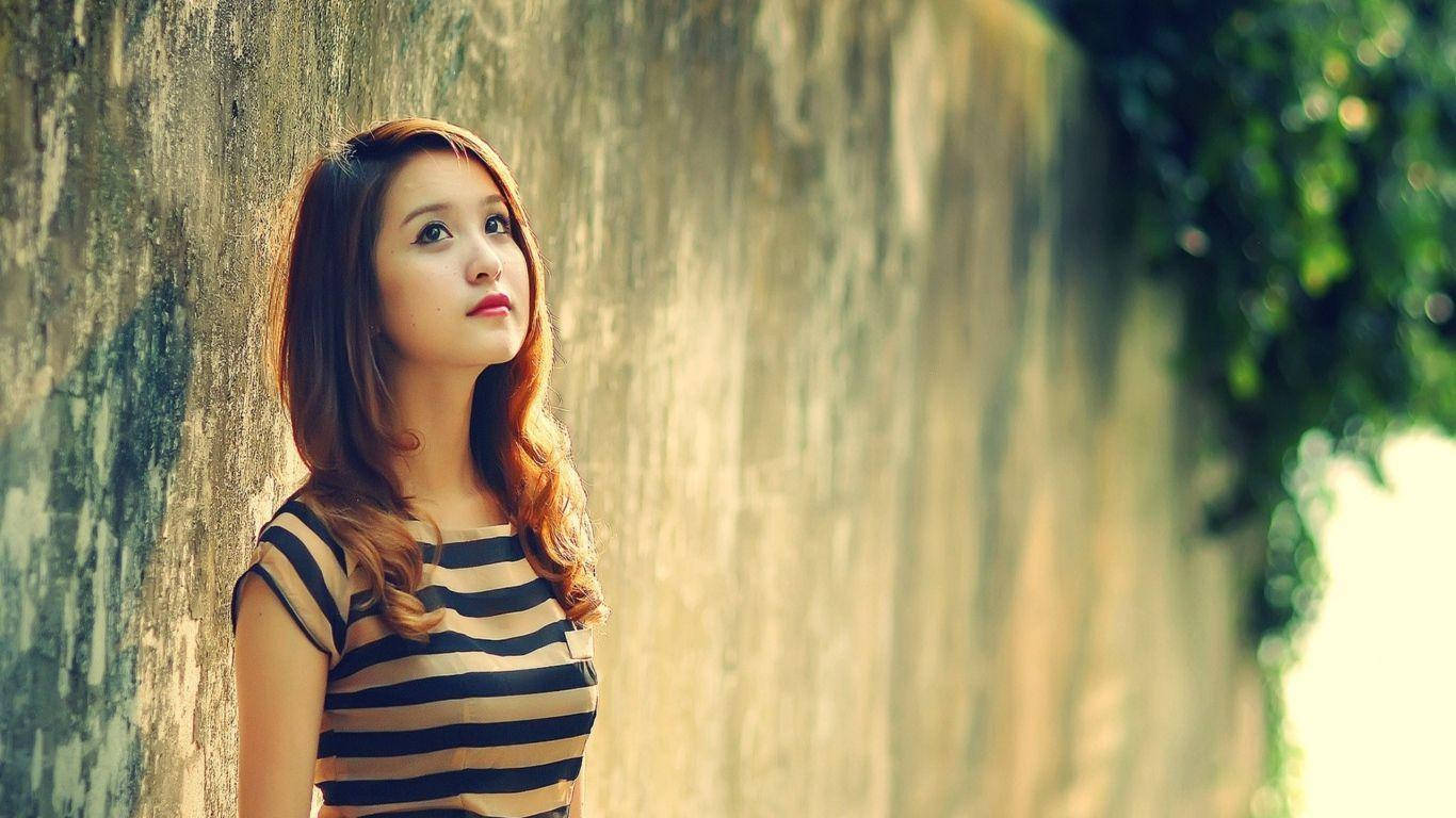 girls 桌布 壁紙 — 一位身穿條紋上衣的年輕女子靠著風化的石牆，背景中的綠植柔和地模糊。