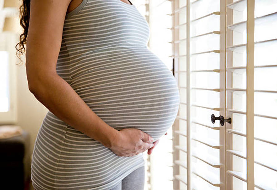 Pregnant 桌布 壁紙 — 一位身穿條紋裙的孕婦在明亮的窗邊輕柔地抱著肚子，窗戶有白色百葉窗。