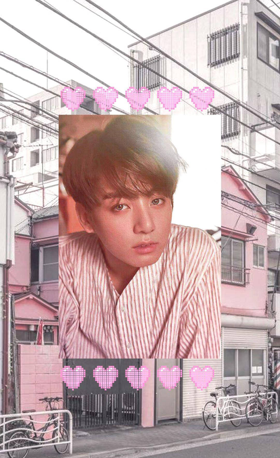 Jungkook Aesthetic 桌布 壁紙 — 一位身穿條紋襯衫的年輕男子位於粉紅色調的城市街道場景中央，像素愛心在上方和下方漂浮。