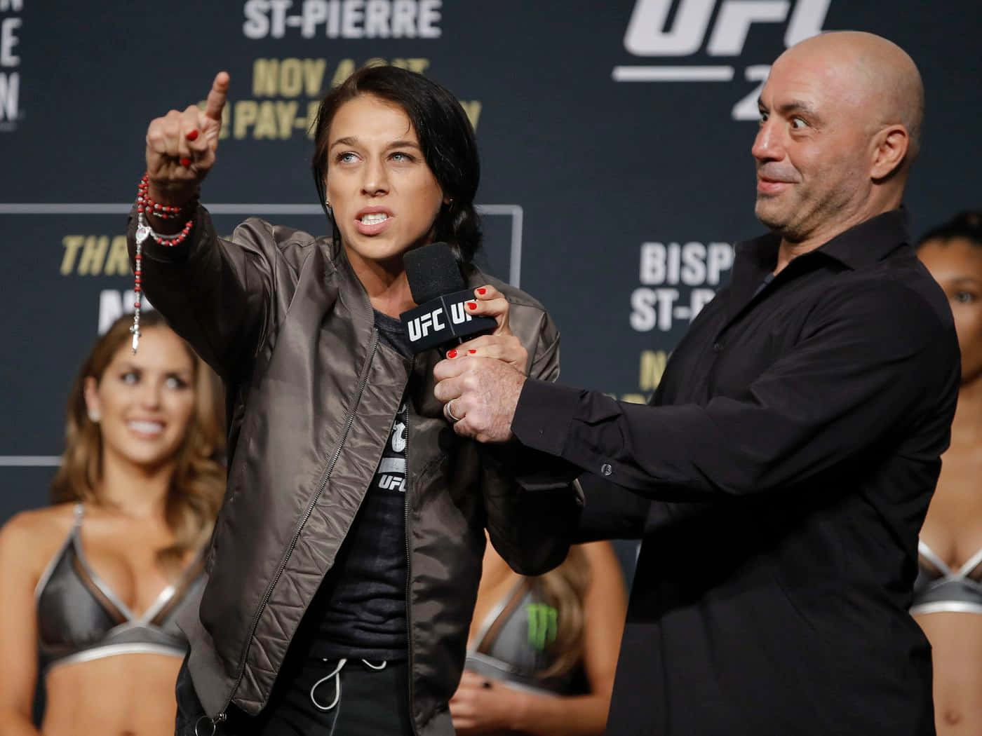 professional 桌布 壁紙 — 一位身穿棕色外套的女性UFC拳手在記者會上接受一位光頭男子手持麥克風採訪時，熱情地做手勢。