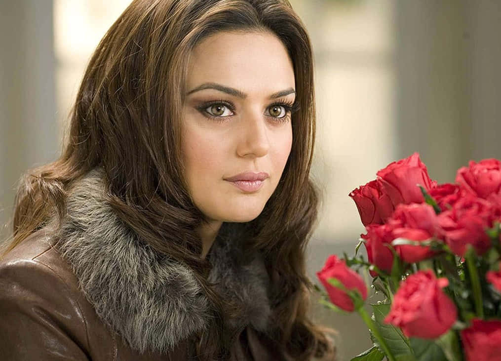 Preity Zinta 桌布 壁紙 — 一位身穿棕色皮草領皮革外套的女性，在鮮豔的紅玫瑰花束旁若有所思地凝視。