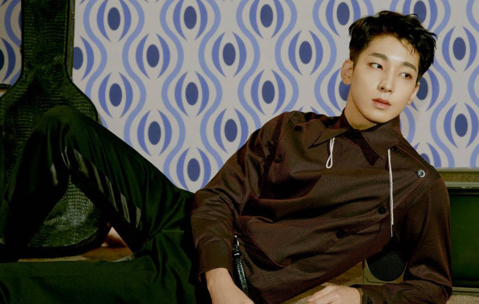 Wonwoo 桌布 壁紙 — 一位身穿棕色質感襯衫的年輕男子，隨意地靠在一張復古藍白圖案壁紙上。