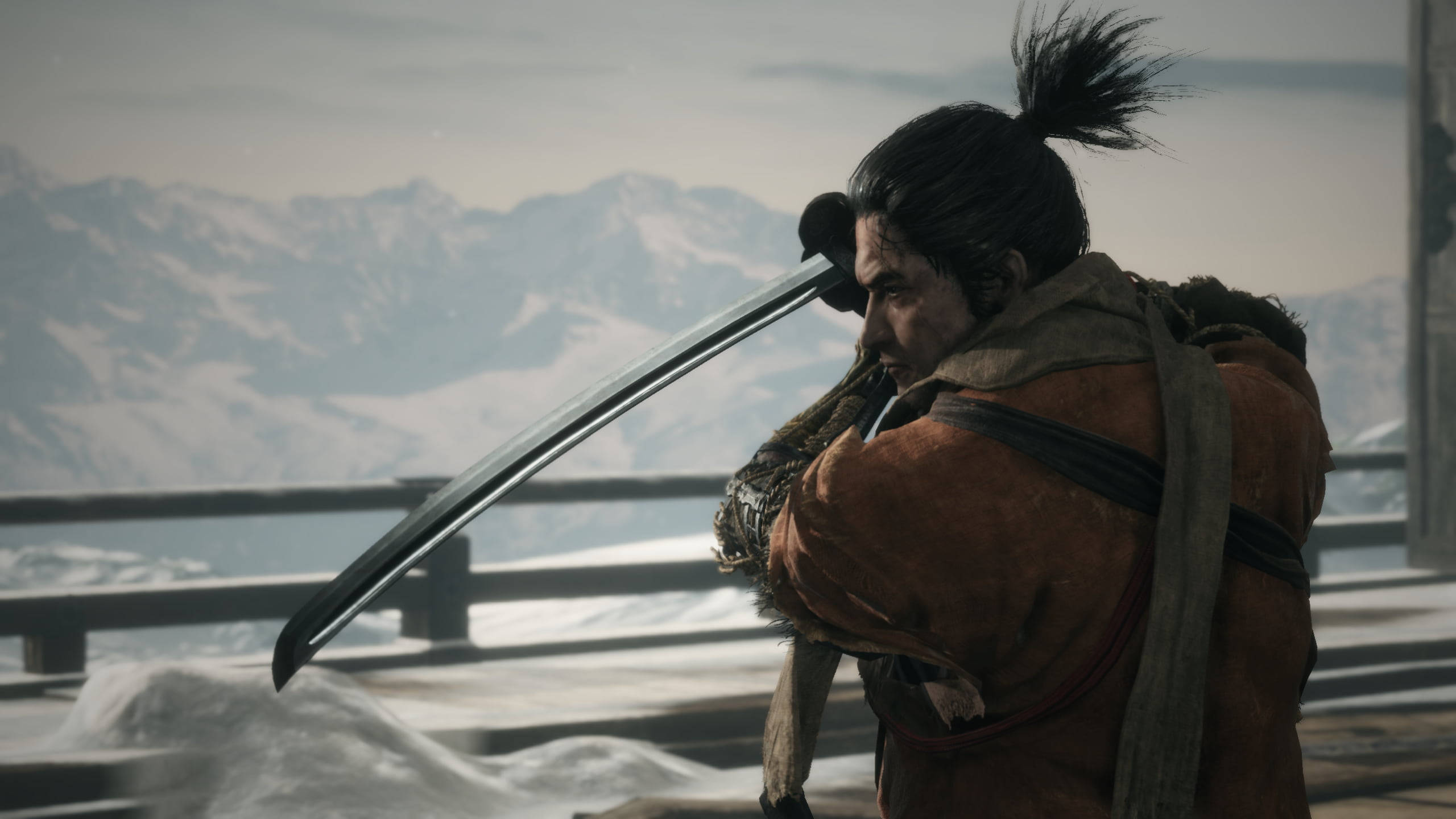 Sekiro 桌布 壁紙 — 一位身穿棕色長袍的武士站在白雪覆蓋的觀景點，手持武士刀，背景是白雪覆蓋的山脈。