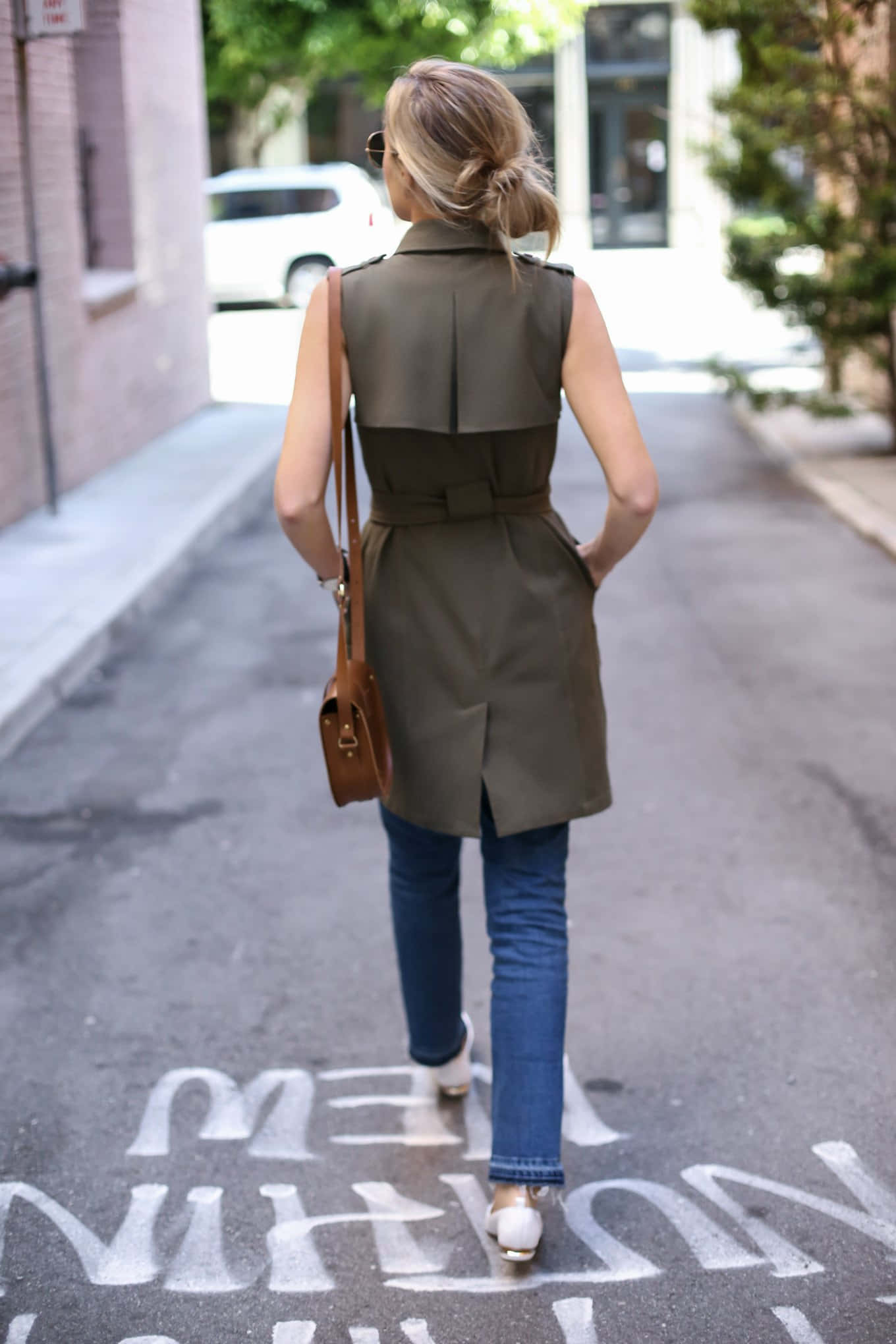 Walking 桌布 壁紙 — 一位身穿橄欖色風衣和牛仔褲的女性沿著一條人行道上有粉筆字的城市街道走開。