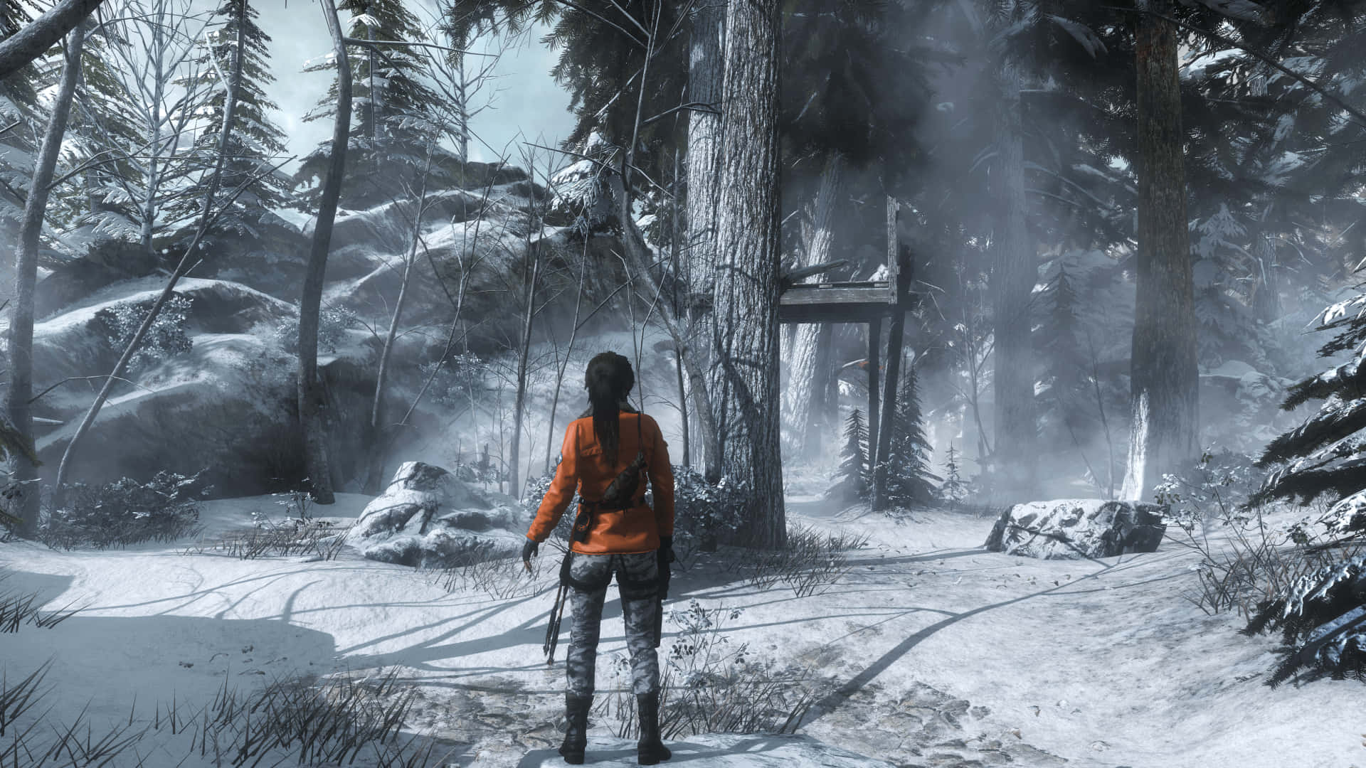 Lara Croft 桌布 壁紙 — 一位身穿橙色外套的孤獨冒險者，走過一片霧氣瀰漫的雪地森林，遠處有一座木結構建築。