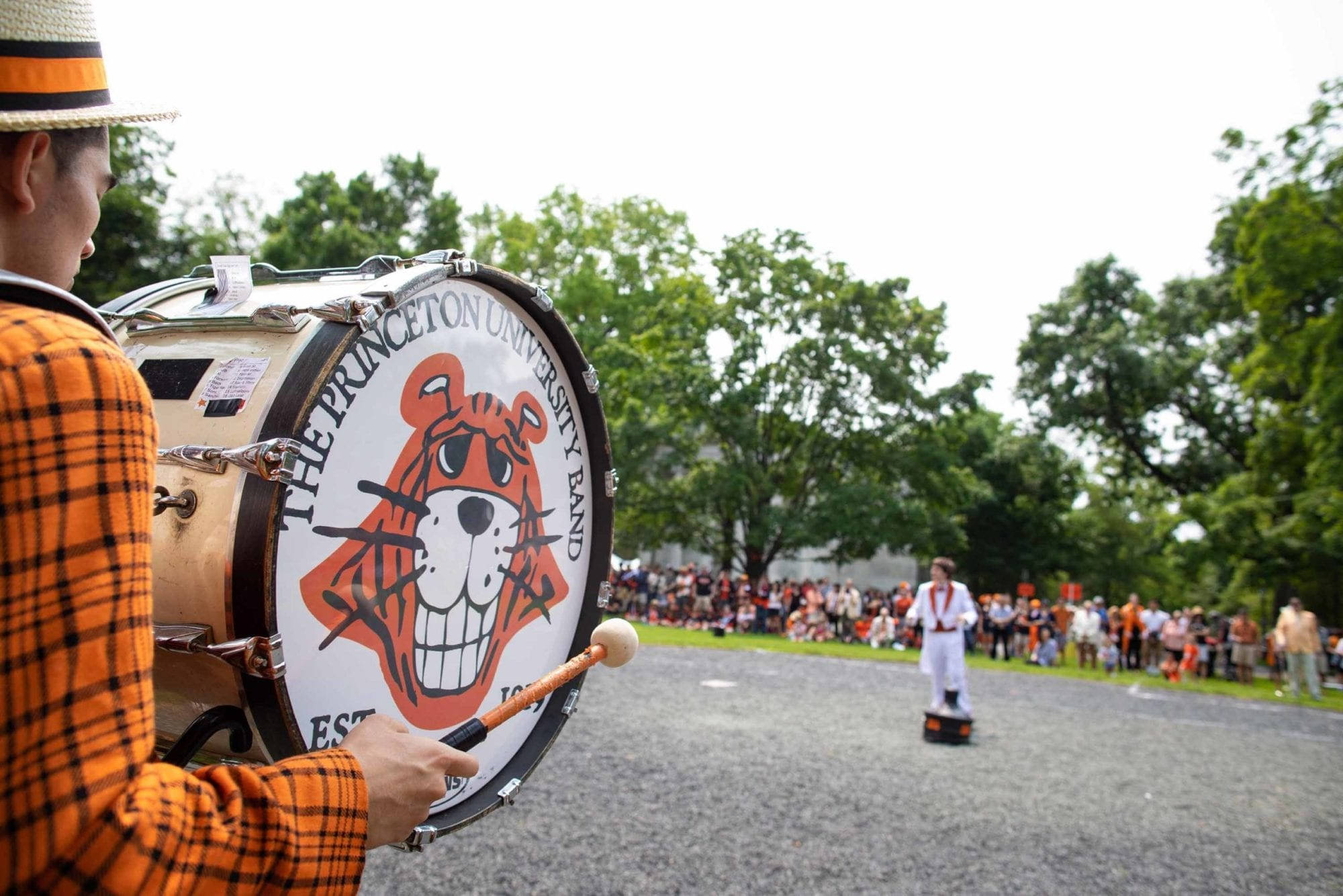 band 桌布 壁紙 — 一位身穿橙色格子圖案的普林斯頓大學樂隊鼓手，在戶外表演中敲擊帶有老虎標誌的低音鼓。