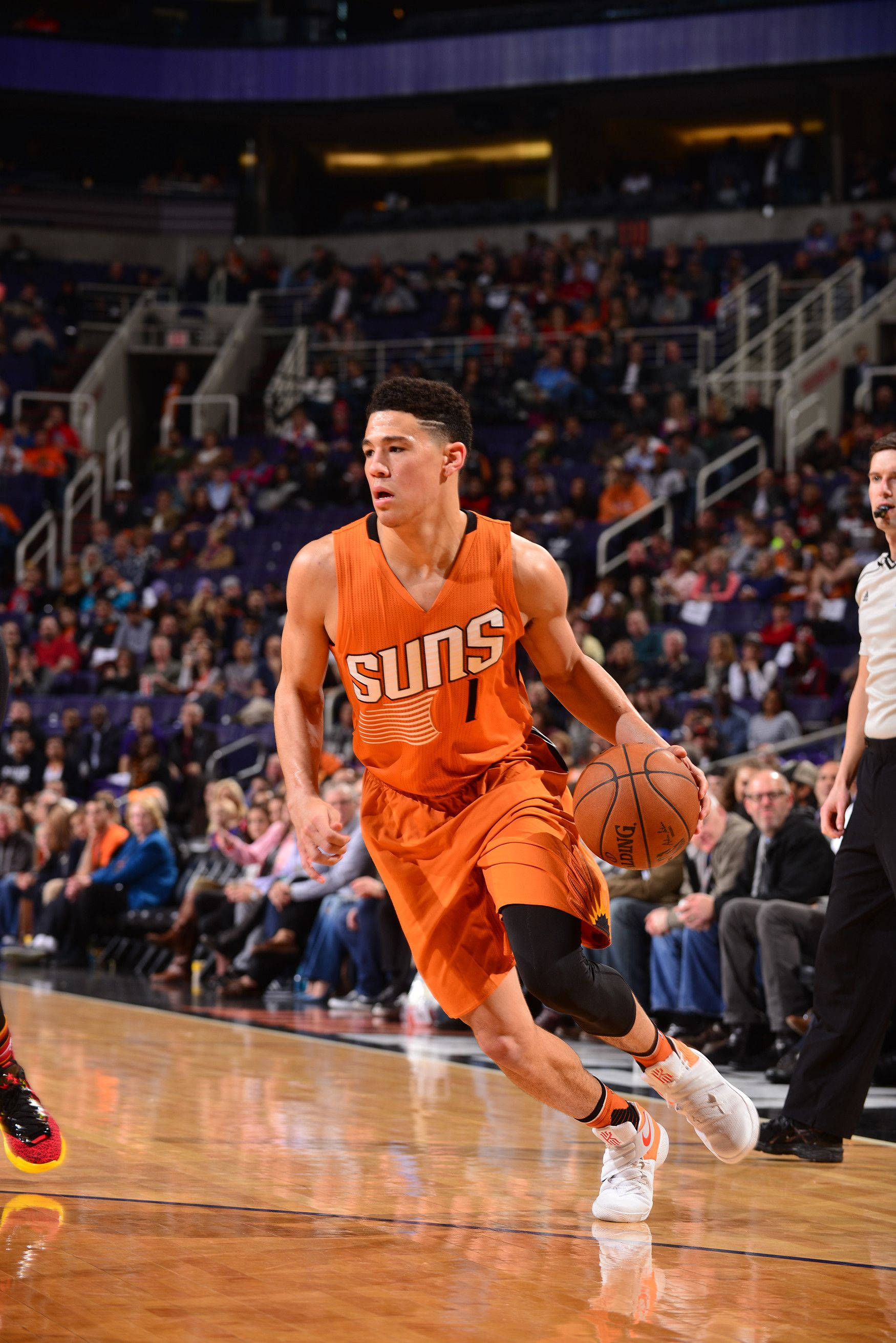 Devin Booker 桌布 壁紙 — 一位身穿橙色球衣的鳳凰城太陽隊籃球運動員在比賽中運球，身後是座無虛席的球館。