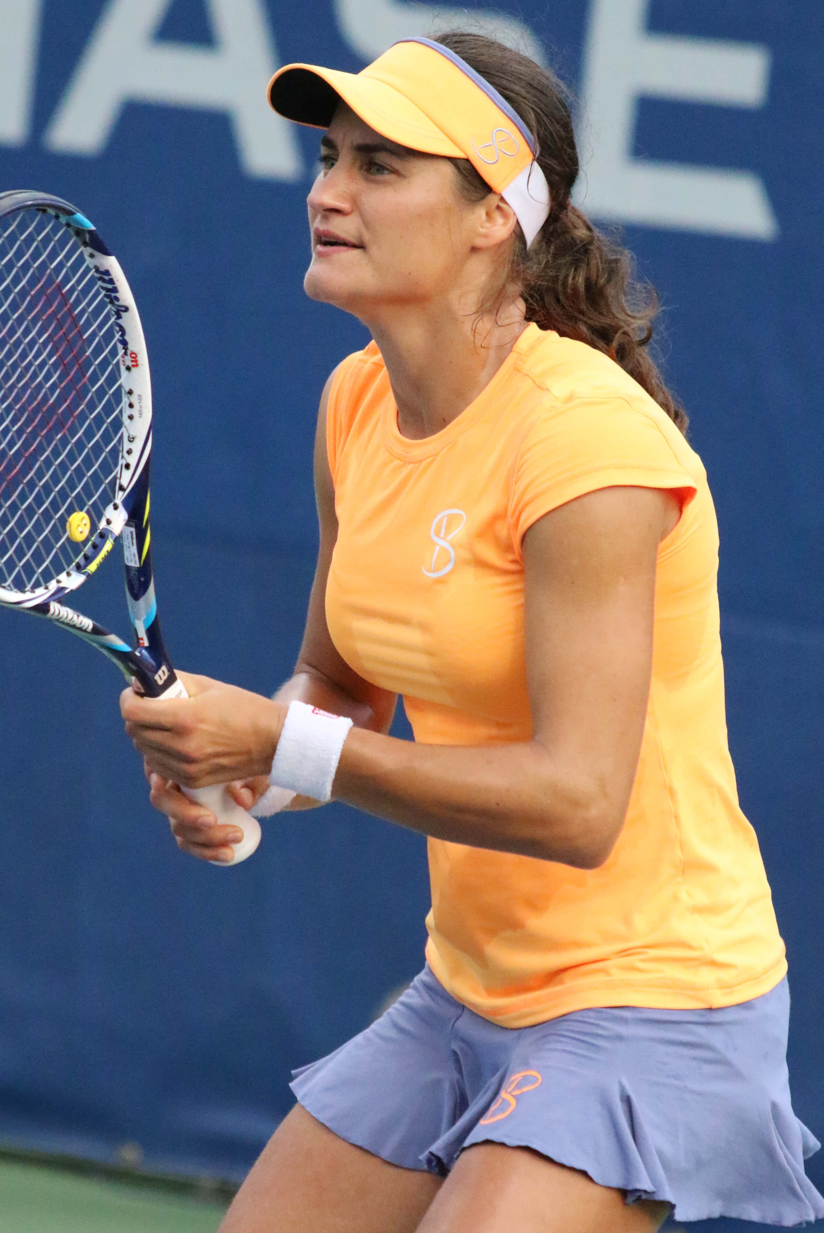 Tennis 桌布 壁紙 — 一位身穿橙色襯衫和藍色裙子的女網球運動員在明亮的日光下準備在硬地球場上擊出正手拍。