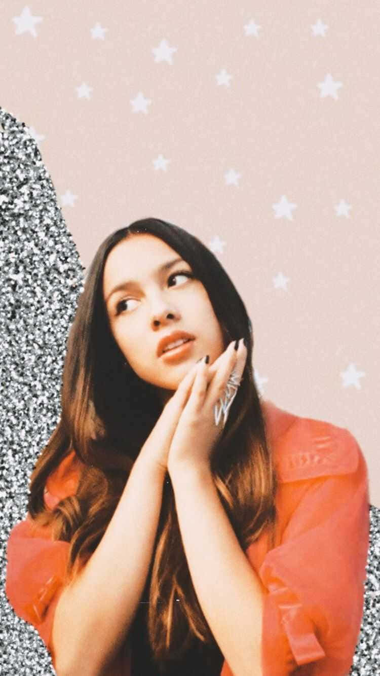 Olivia Rodrigo Aesthetic 桌布 壁紙 — 一位身穿橙色襯衫的年輕女性，在帶有閃亮銀色點綴的粉紅色星空背景下向上凝視。