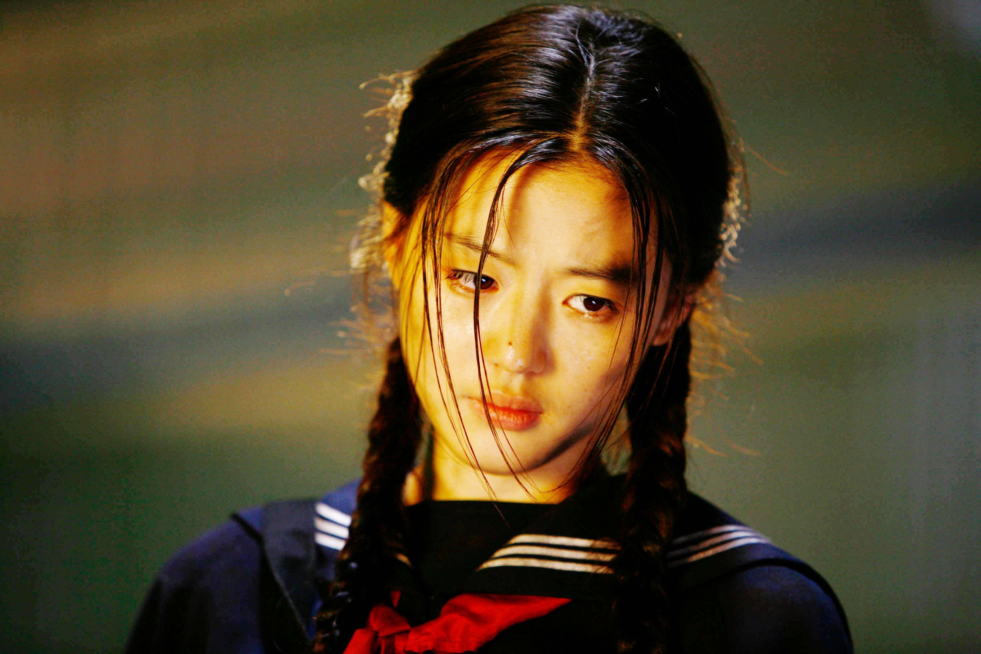 Jun Ji Hyun 桌布 壁紙 — 一位身穿水手服、濕辮子頭髮的年輕女性在溫暖燈光下專注地凝視。