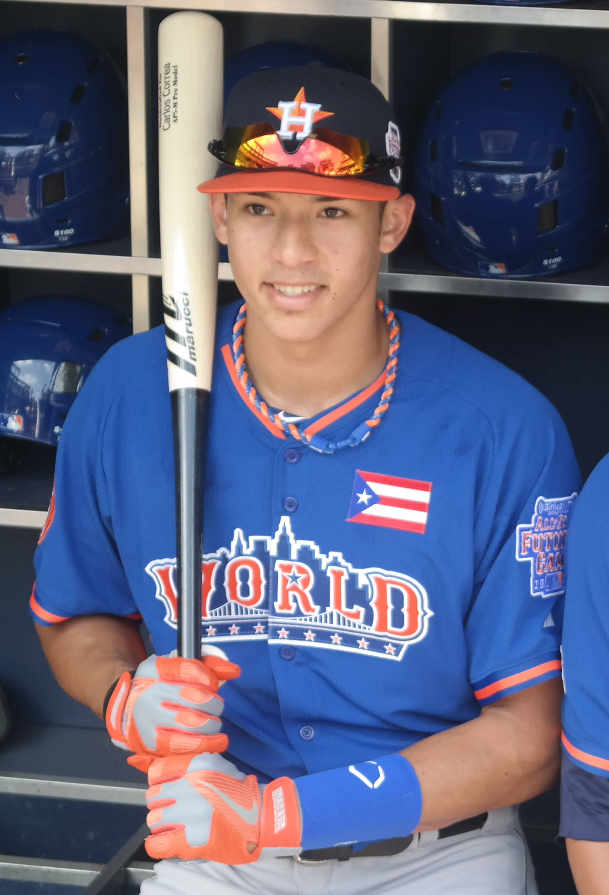 Carlos Correa 桌布 壁紙 — 一位身穿波多黎各世界棒球經典賽藍色球衣的年輕棒球運動員在頭盔環繞的休息區微笑著拿著球棒。