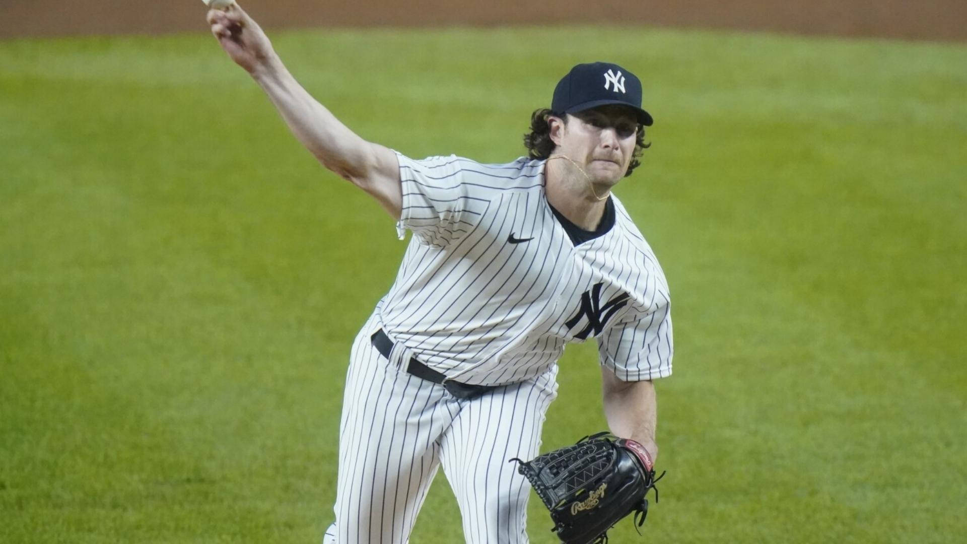 Gerrit Cole 桌布 壁紙 — 一位身穿洋基條紋球衣的棒球投手在體育場燈光下，於充滿活力的綠色球場上準備投球。