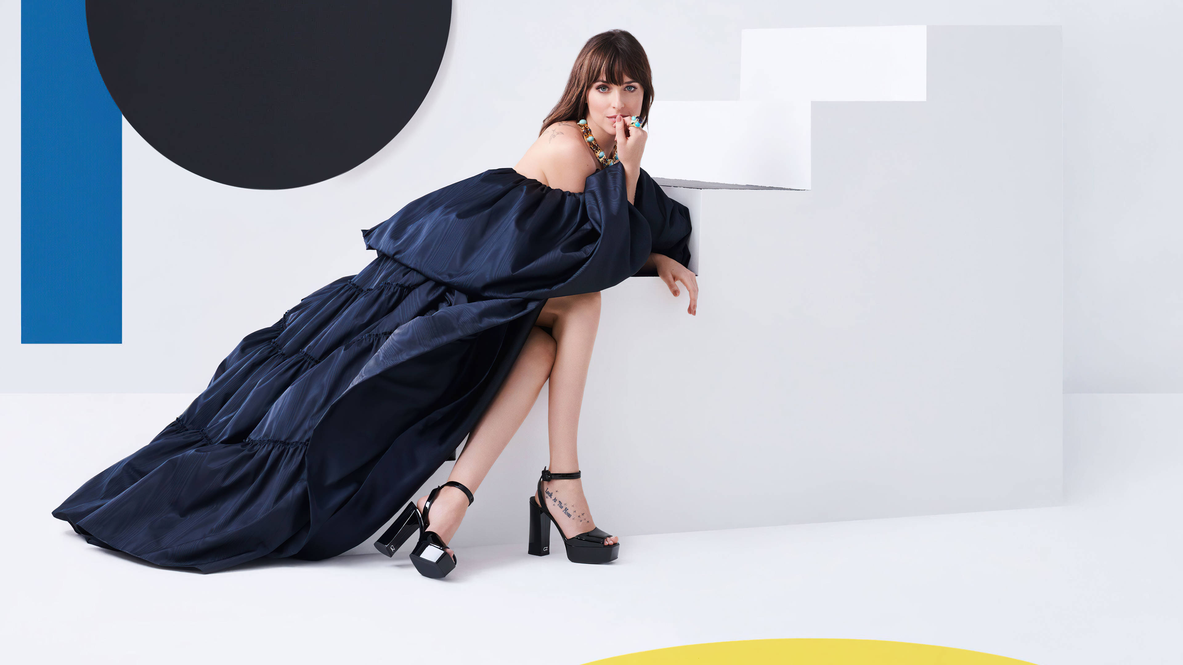 Dress 桌布 壁紙 — 一位身穿海軍藍寬鬆長裙的女性，在極簡白色牆壁前優雅擺姿勢，牆上有藍色、黑色和黃色的醒目幾何形狀。