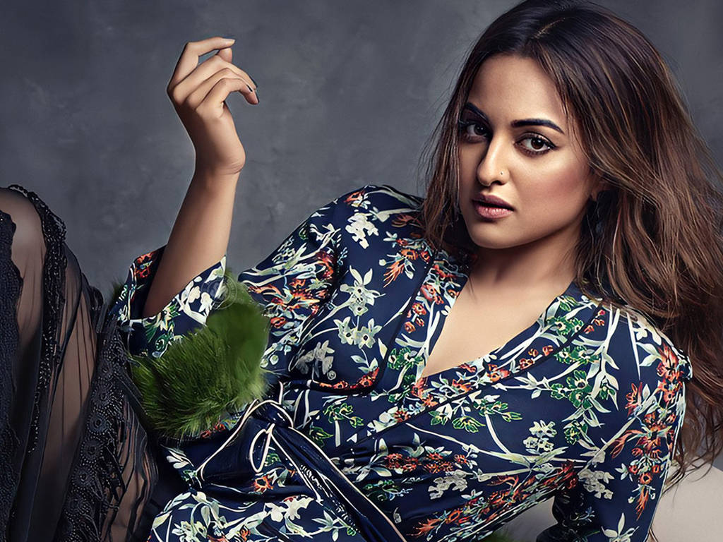 Sonakshi Sinha 桌布 壁紙 — 一位身穿海軍藍花卉連衣裙、搭配綠色毛皮裝飾的女性，在紋理灰色背景前自信地擺姿勢。