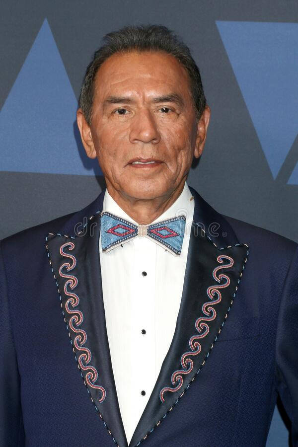 actor 桌布 壁紙 — 一位身穿海軍藍西裝、飾有精緻紅白刺繡和圖案領結的尊貴男士，在幾何藍色背景前擺姿勢。