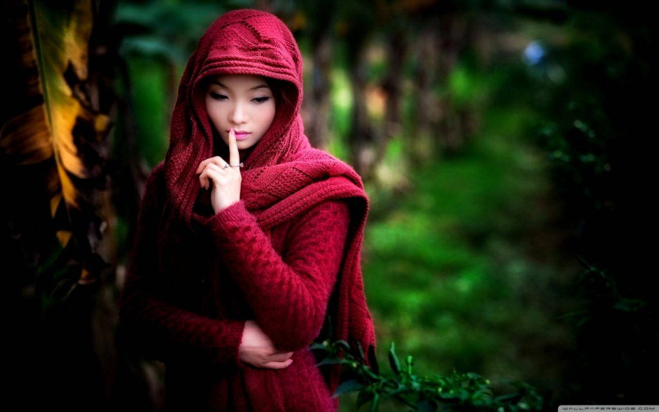 girls 桌布 壁紙 — 一位身穿深紅色針織連帽毛衣的女性站在茂密的綠色森林中，將手指放在嘴唇上做出安靜的手勢。