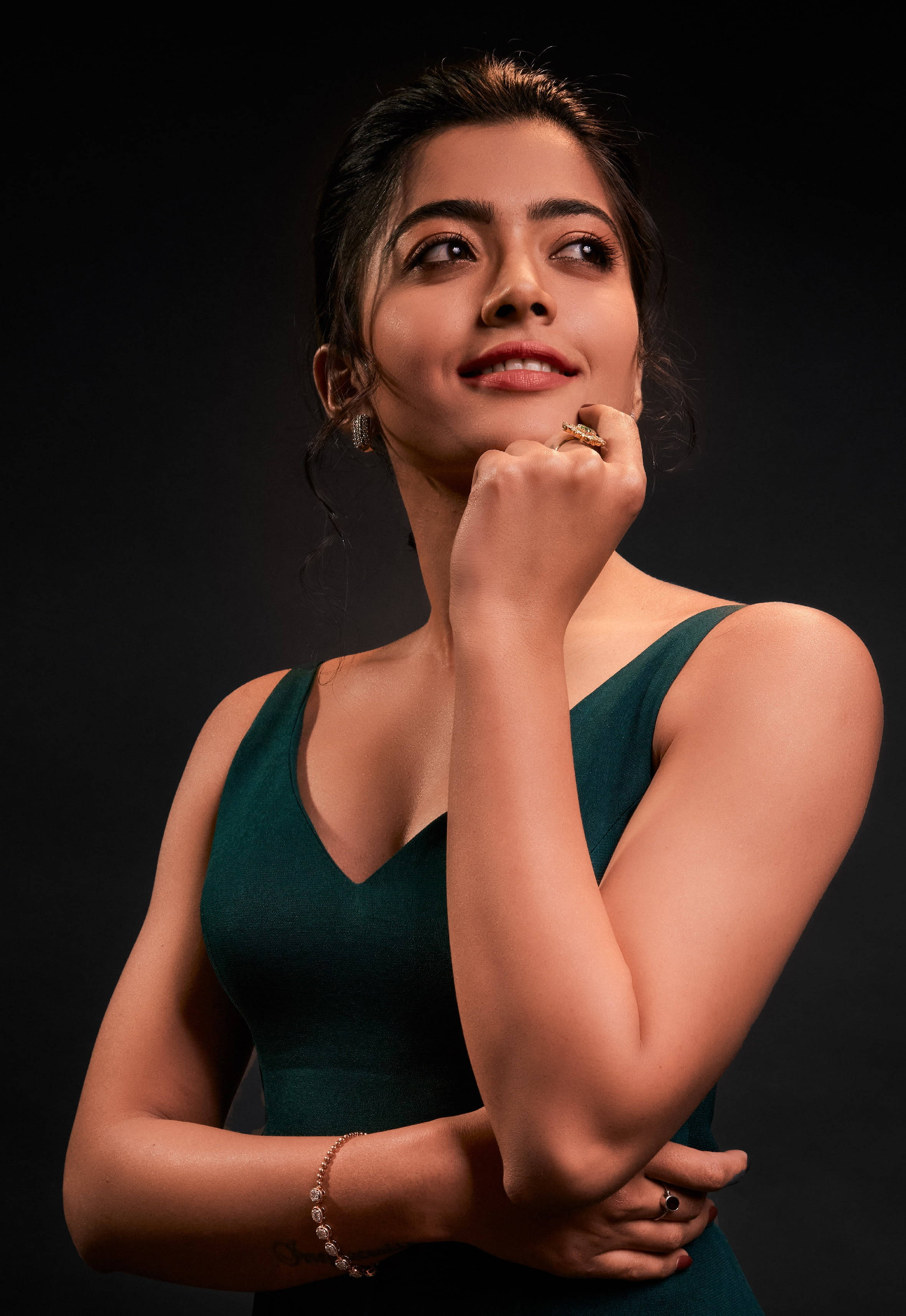 telugu 桌布 壁紙 — 一位身穿深綠色連衣裙的女性在黑色背景下抬頭仰望，帶著若有所思的微笑。
