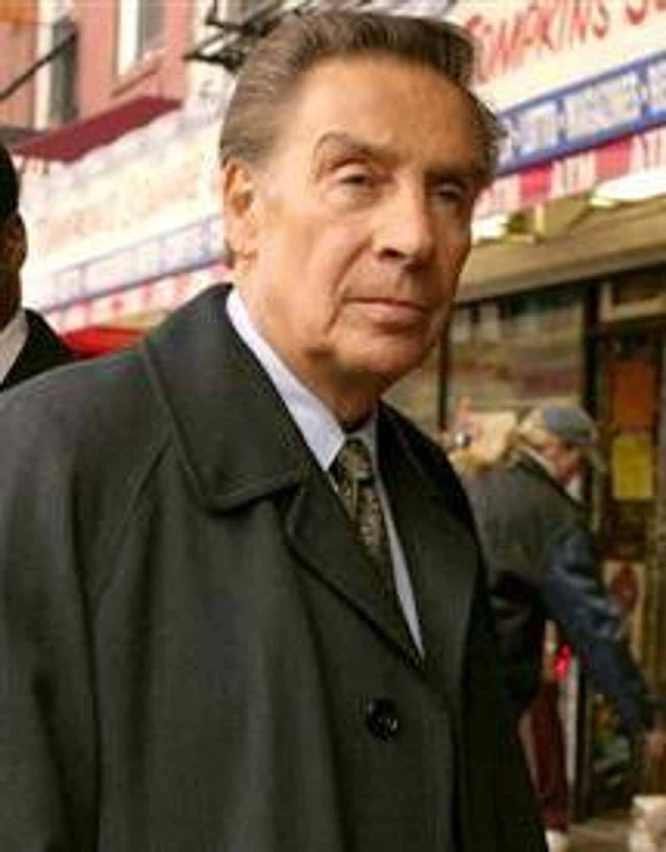 actor 桌布 壁紙 — 一位身穿深色外套和領帶的年長男子站在繁忙的城市街道上，身後有商店和行人。
